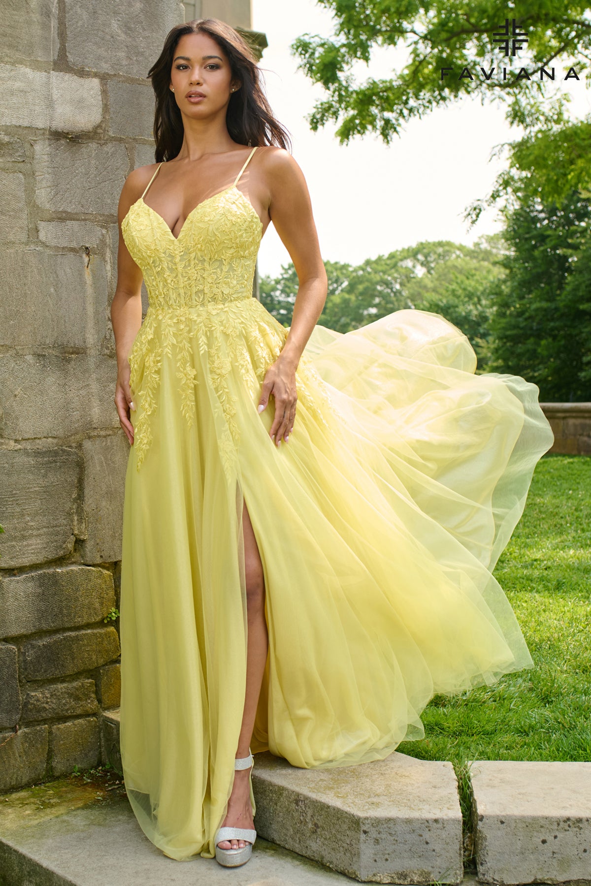 Woman in a yellow evening gown standing outdoors near a stone wall.