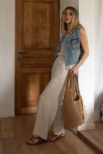 Woman wearing Light Beige Luxe Pants by Molly Bracken paired with denim vest and carrying woven bag indoors