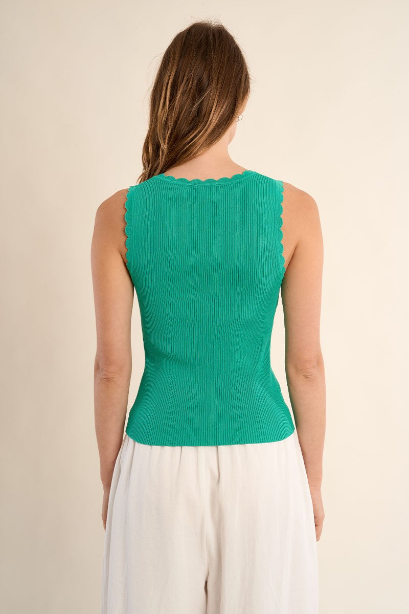 Back view of a woman wearing a ribbed Mint Tank Top by Molly Bracken with scalloped edges and white pants.