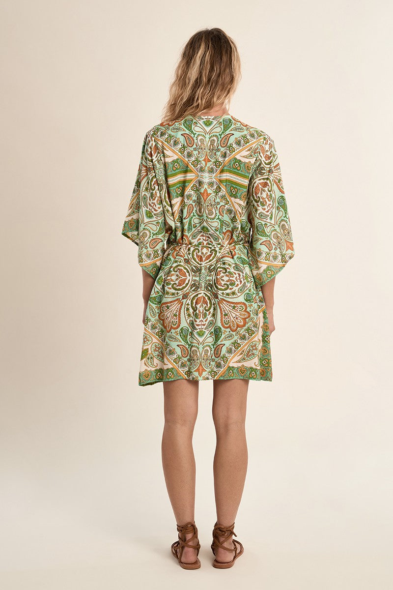 Woman wearing a patterned Green Ines Dress by Molly Bracken standing with back to camera against beige background