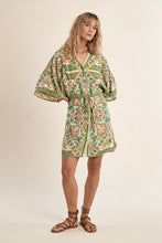Woman wearing a patterned Green Ines Dress by Molly Bracken with billowy sleeves and a cinched waist, paired with brown sandals
