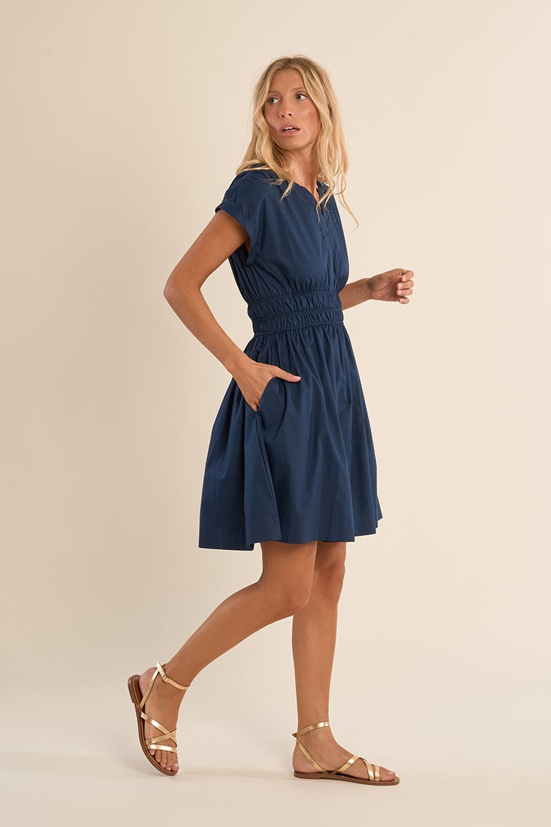 Woman wearing Navy Blue Harbor Dress by Molly Bracken with short sleeves and gathered waist, paired with gold sandals