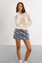Model wearing Molly Bracken White Petal Knit Sweater with floral denim skirt in a casual pose against white wall