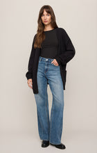 Woman wearing Black Sanborn Cardigan by z supply with black shirt and blue jeans against beige background