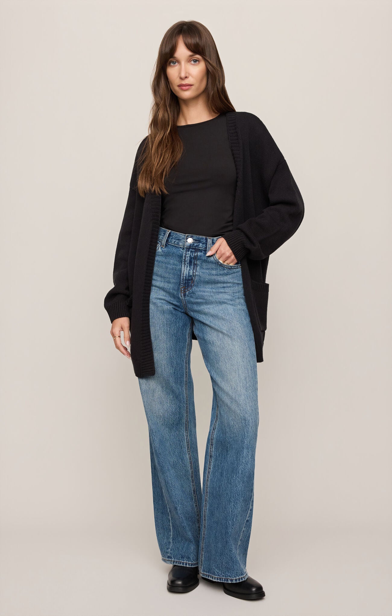 Woman wearing Black Sanborn Cardigan by z supply with black shirt and blue jeans against beige background