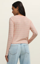 Woman with dark hair wearing a washed pink and cream striped long-sleeve Henley top and light blue jeans facing away