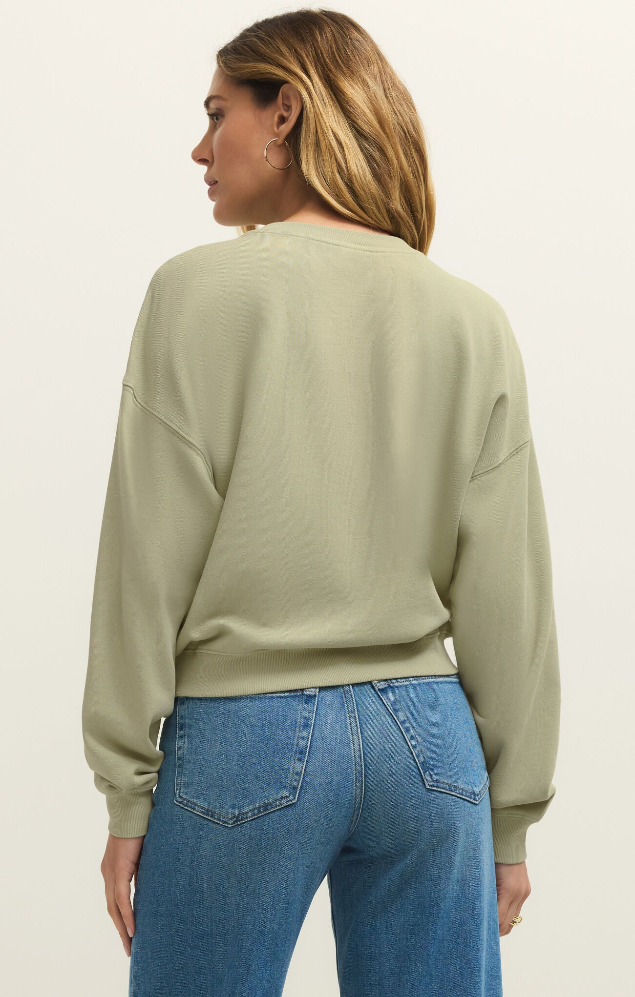 Woman with shoulder-length hair wearing a light green sweatshirt and blue jeans standing facing away from the camera
