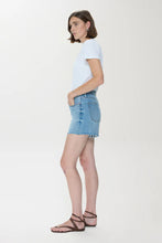 Side view of a woman wearing Pistola Kennedy Short denim skirt styled with a white tee and brown sandals