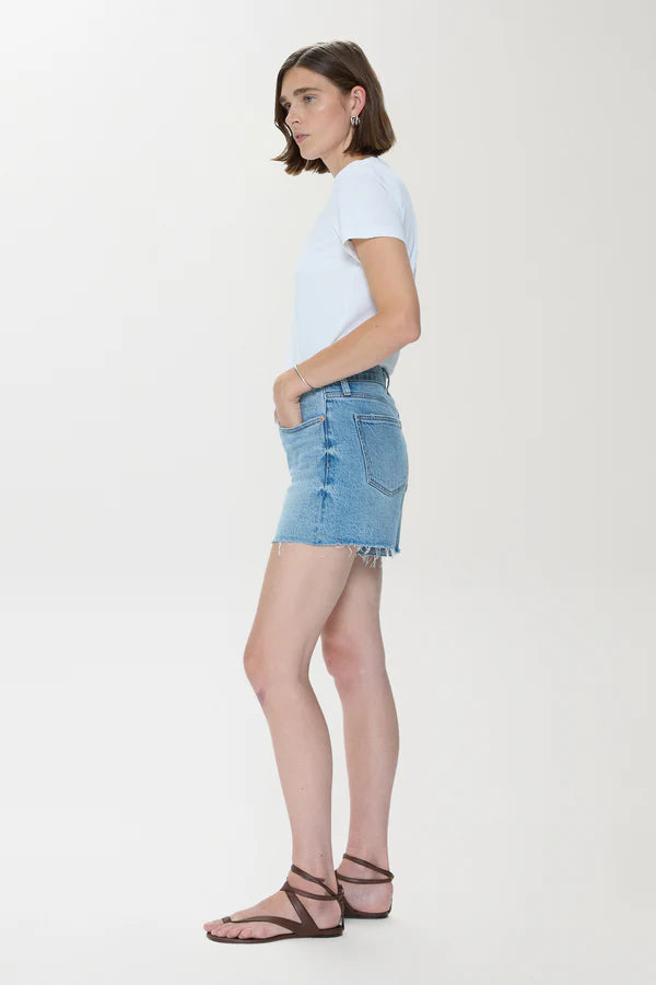 Side view of a woman wearing Pistola Kennedy Short denim skirt styled with a white tee and brown sandals
