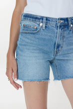 Close-up of light blue denim Pistola Kennedy Short with raw hem worn by a person standing against white background