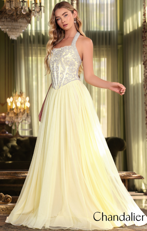 Blonde woman wearing a yellow embellished halter prom dress standing in an elegant room with chandeliers