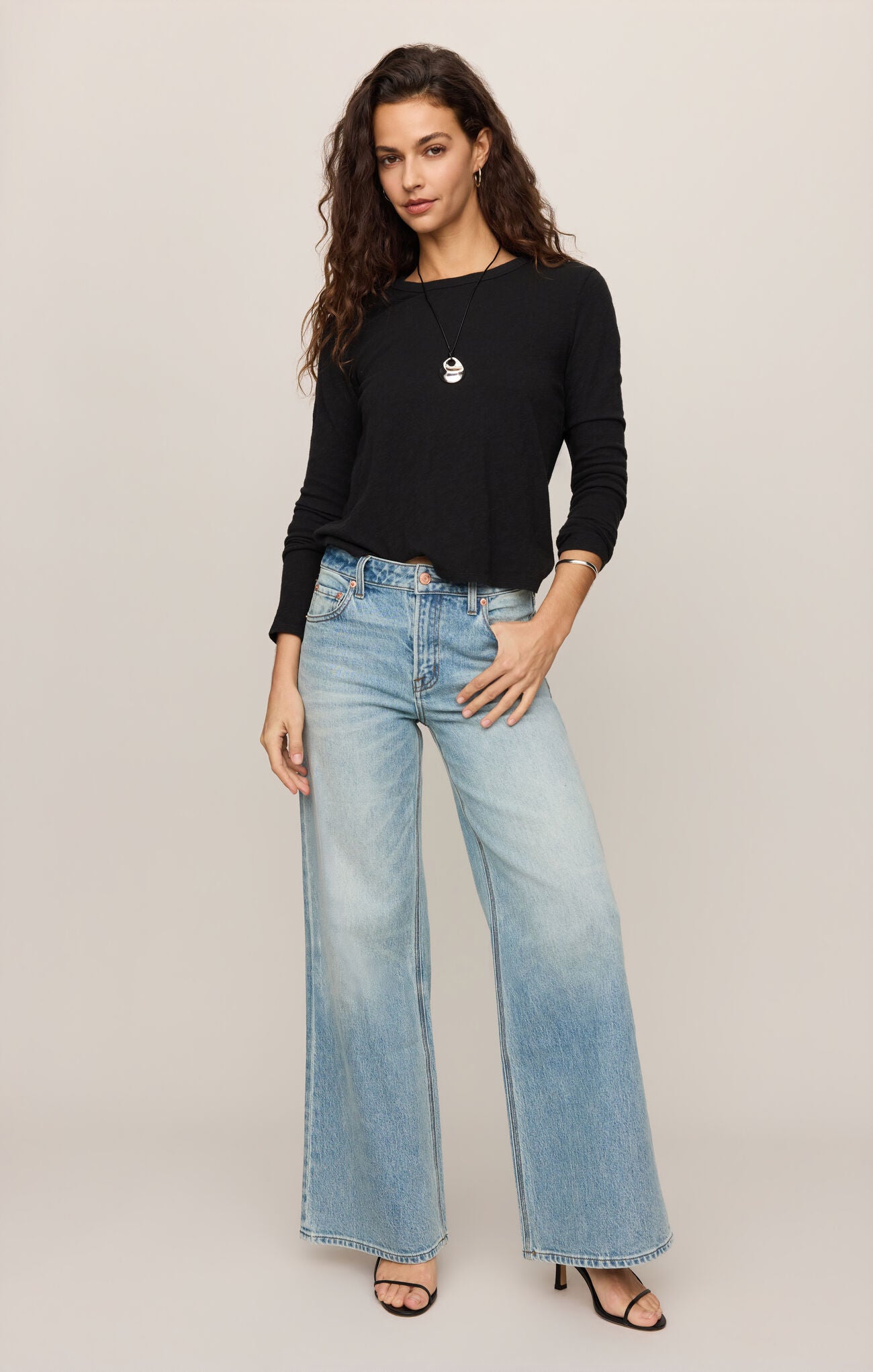 Woman wearing black Junie Long Sleeve Tee by z supply with light blue wide-leg jeans and sandals posing