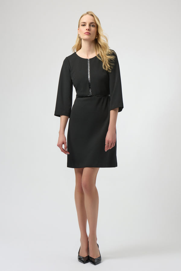 Woman with long blonde hair wearing a black scuba crepe A-line dress with three-quarter bell sleeves standing against a white background