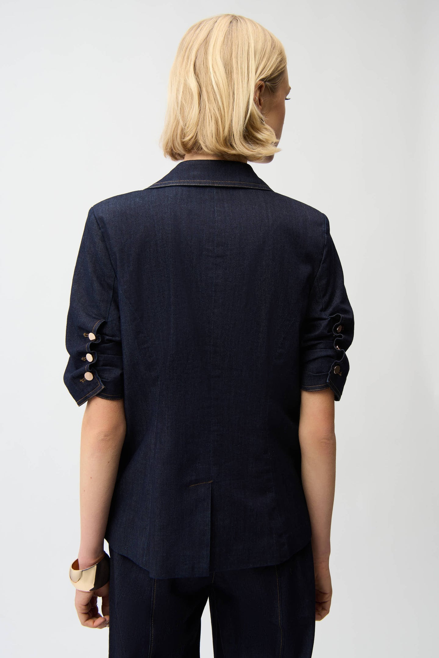 Back view of a woman wearing Joseph Ribkoff Dark Blue Denim Fitted Blazer with ruched sleeves and buttons by JOSEPH Ribkoff