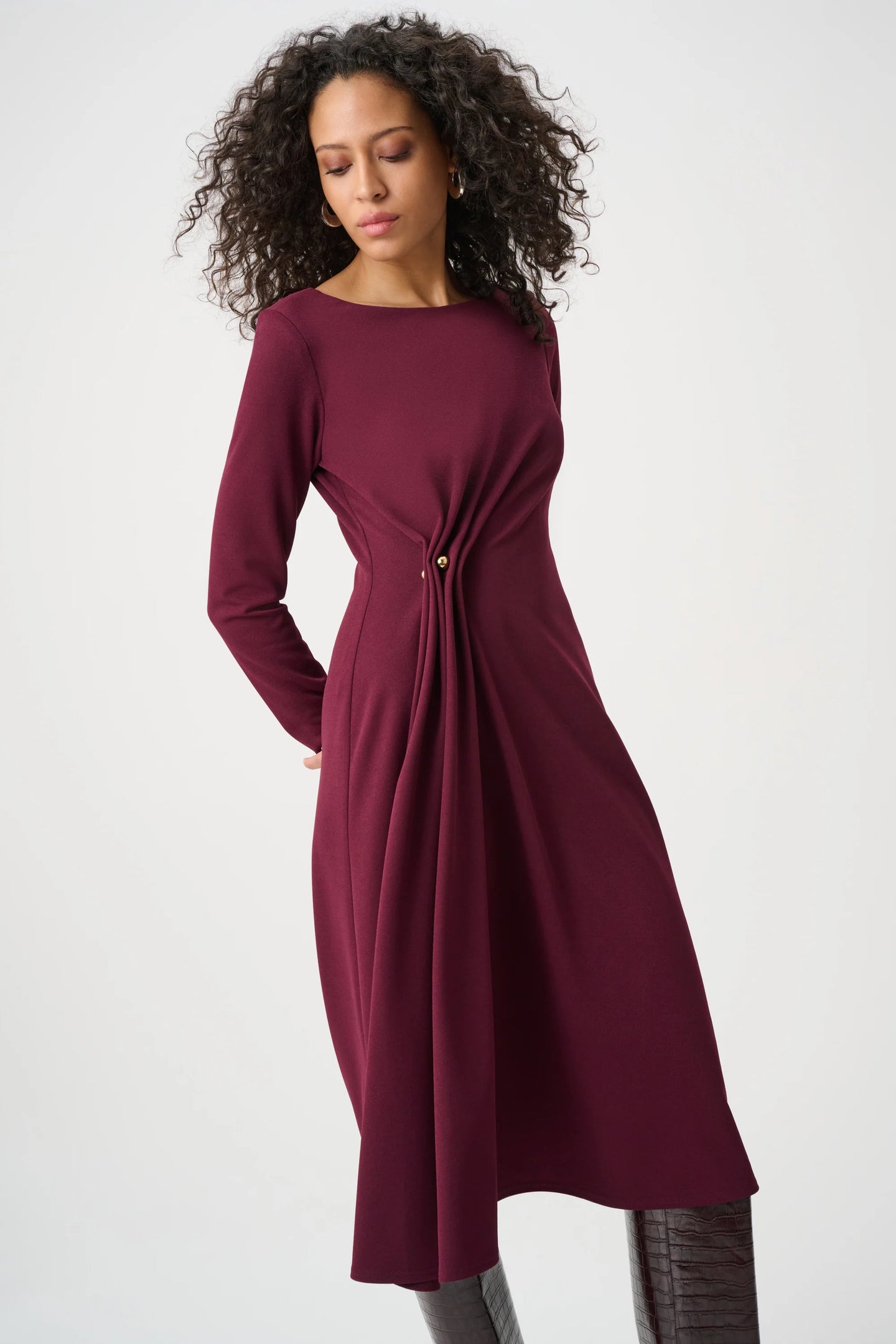 Woman wearing a burgundy long sleeve draped dress with a gathered waist and flowing skirt