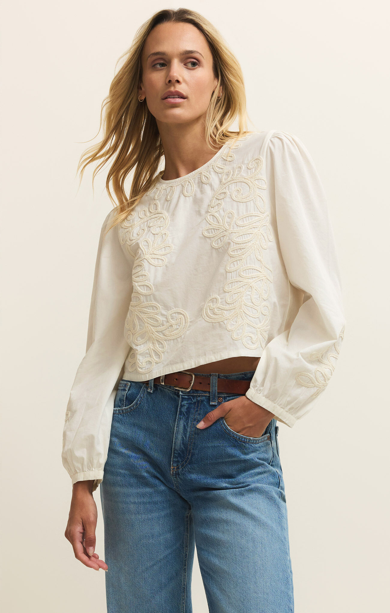 Woman wearing White Tatiana Poplin Top by z supply with long sleeves and intricate embroidery paired with jeans