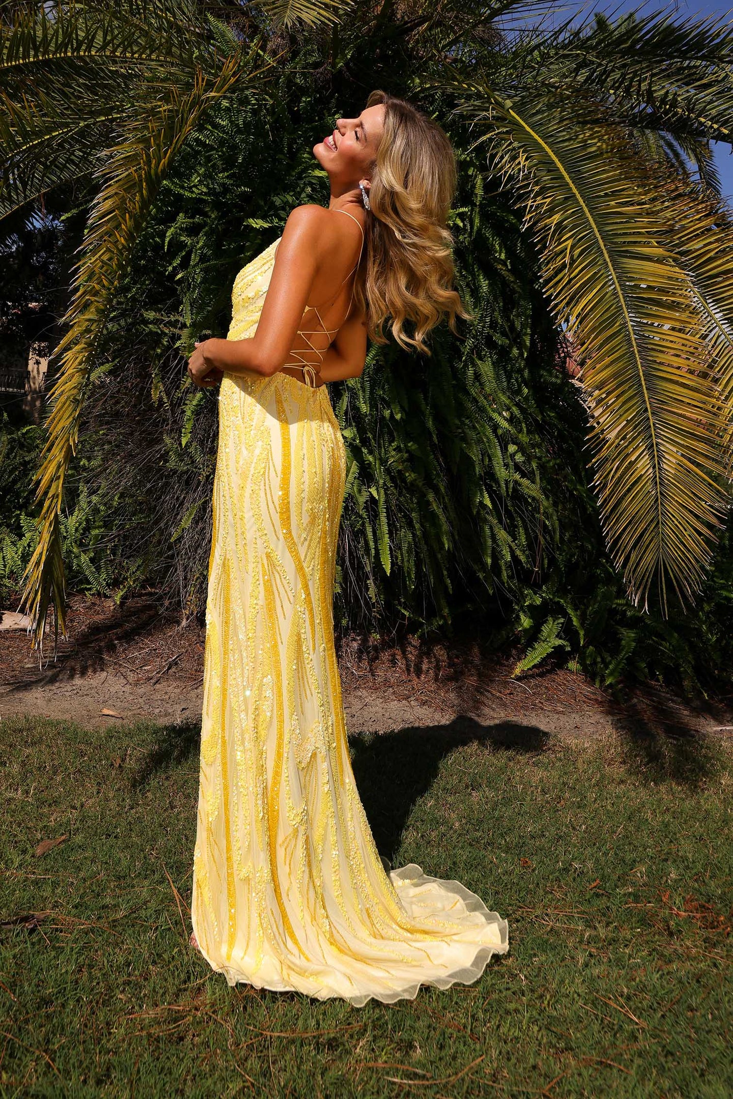 Woman outside wearing yellow sequined Primavera Prom Dress Style 4513 with open back and flowing skirt in sunlight