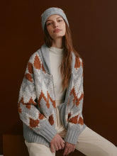 Woman with long brown hair wearing a grey and rust patterned knit jacket and matching headband sitting against a brown background