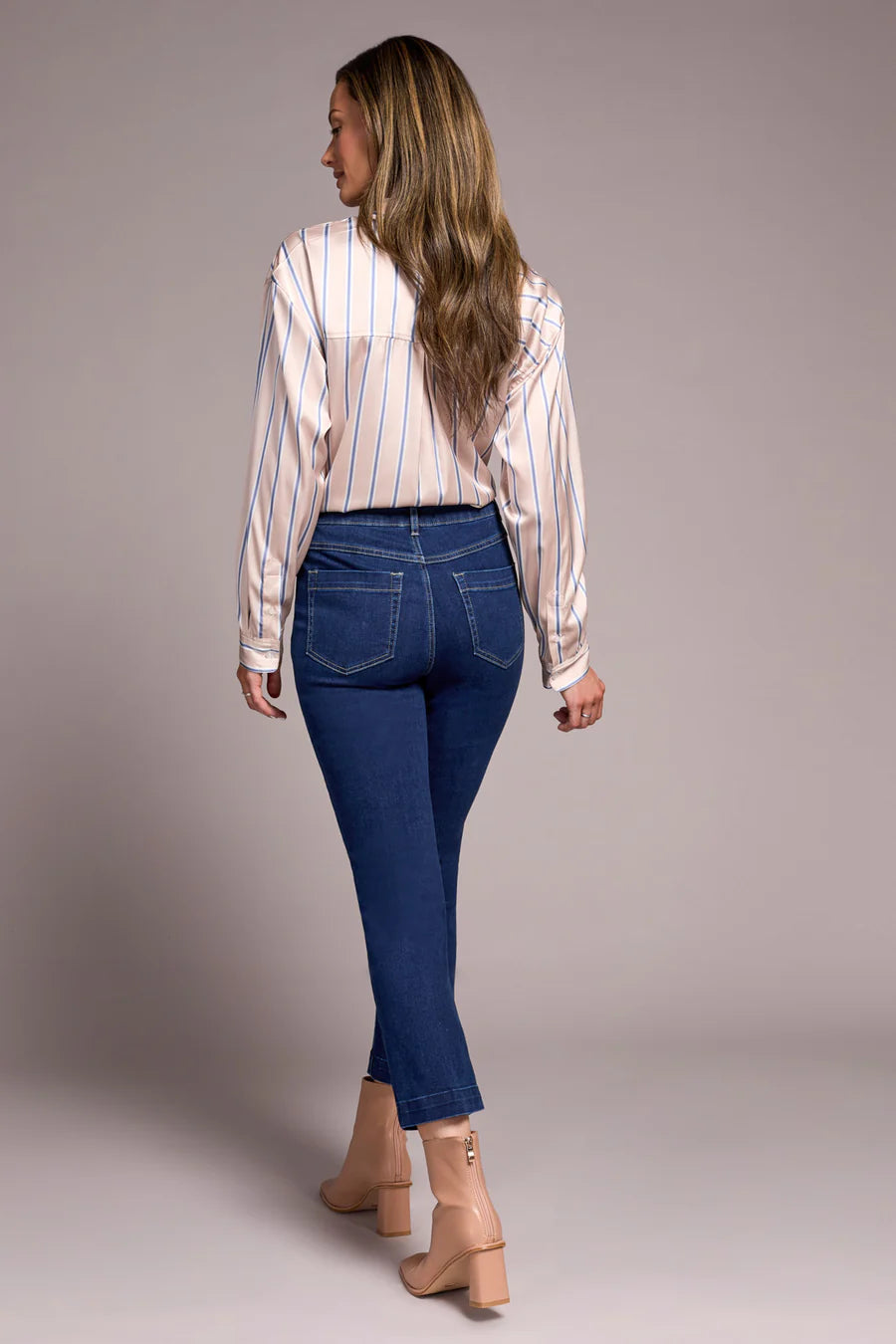 Woman wearing Tribal Audrey Pull-On Crop Straight Jeans with Front Crease in dark denim facing away against plain background