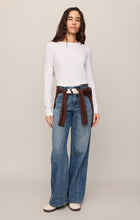 Woman wearing a white Junie Long Sleeve Tee by z supply paired with wide-leg jeans and a brown sweater tied at waist