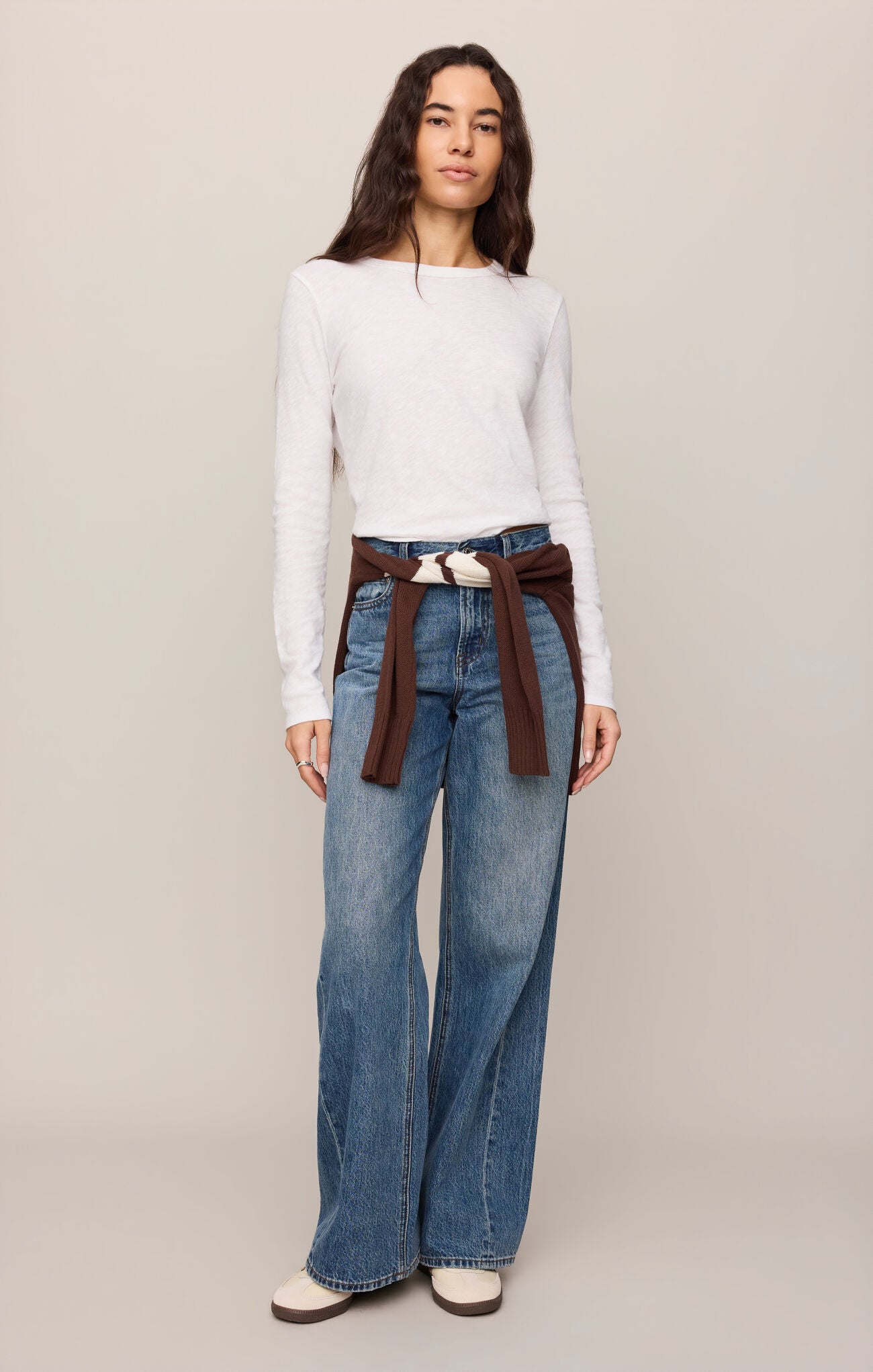 Woman wearing a white Junie Long Sleeve Tee by z supply paired with wide-leg jeans and a brown sweater tied at waist