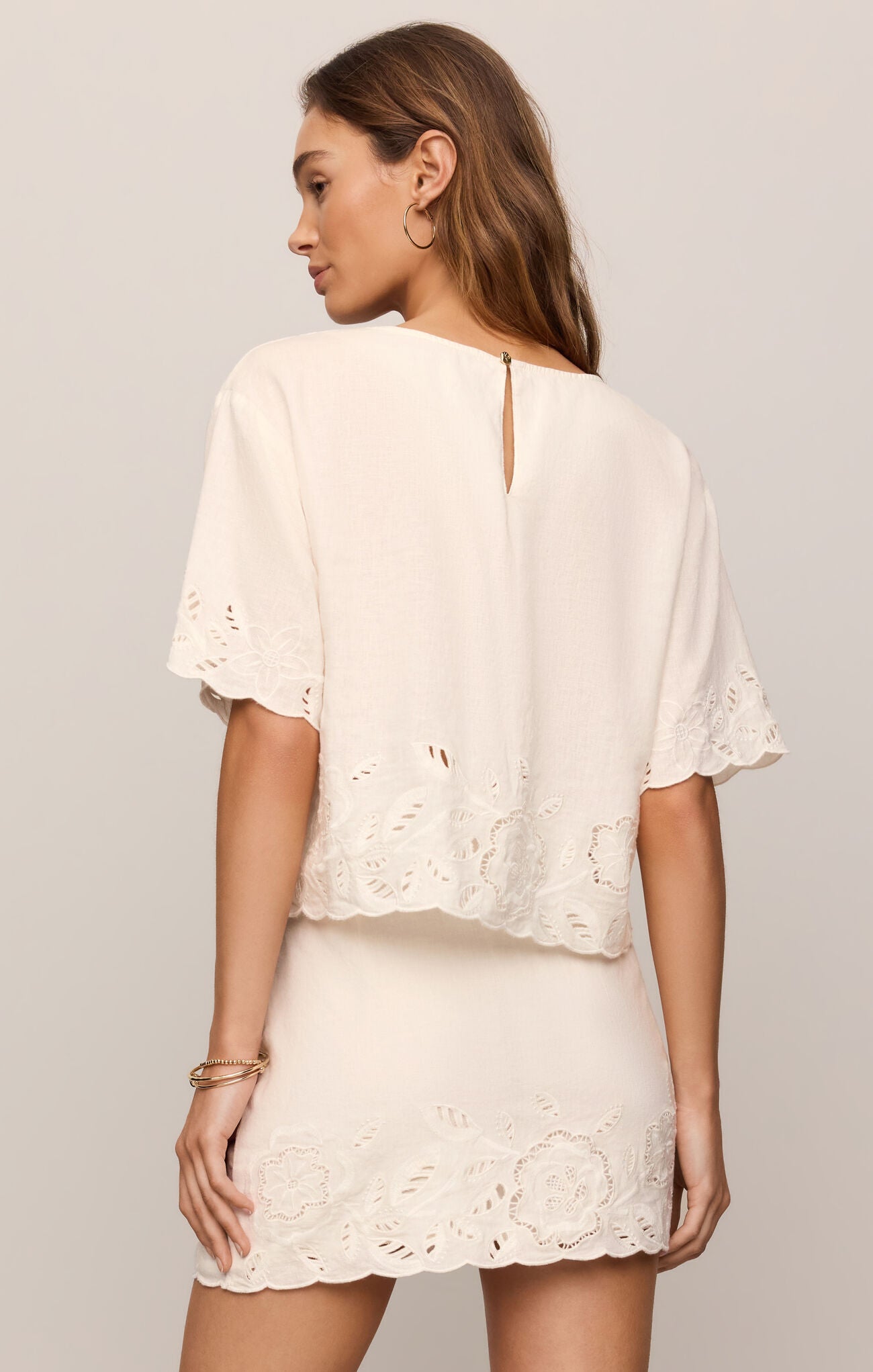 Woman wearing a White Daya Embroidered Top by z supply with floral cutout details on sleeves and hem