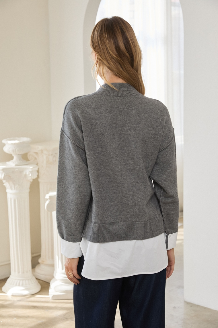 Woman viewed from behind wearing a gray sweater over a white shirt in a bright classical interior