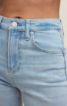 Close-up of light blue high-rise wide leg jeans worn by a person showing front pocket and button details