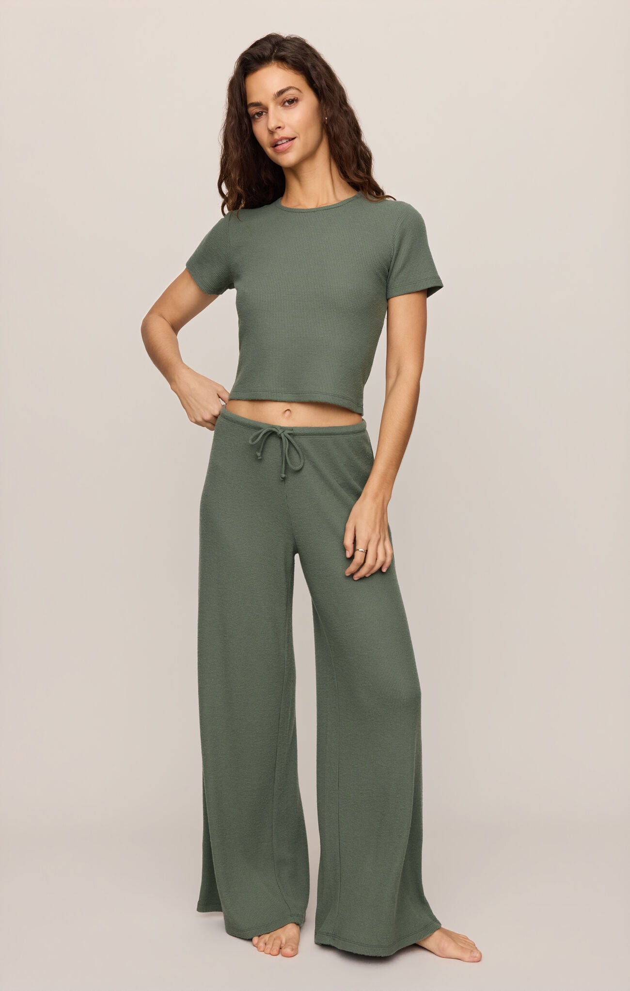 Woman wearing olive green Monstera Waffle Tee and matching wide-leg pants by z supply, standing against beige background
