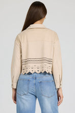 Back view of a woman wearing a beige Dear John Retta Jacket with laser-cut detailing above the hem and light blue jeans