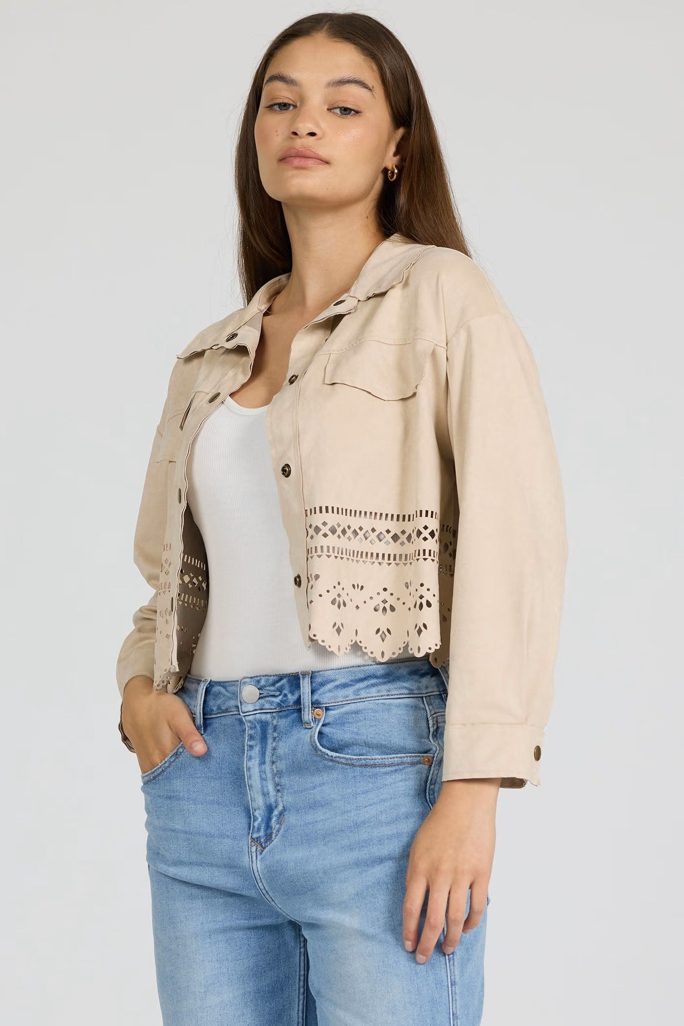Woman wearing a beige cropped jacket with laser-cut detailing and button closure, styled with jeans and white top, Dear John Retta Jacket