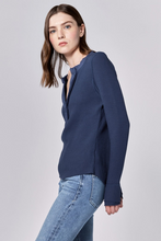 Woman wearing dear john Black Iris Luna Top in navy blue textured fabric paired with light blue jeans on gray background