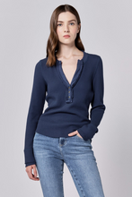 Woman wearing fitted long sleeve Black Iris Luna Top by dear john with a v-neck and casual blue jeans standing against gray background