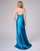 Blonde woman wearing a strapless teal prom dress with a fitted bodice and flowing skirt standing facing away