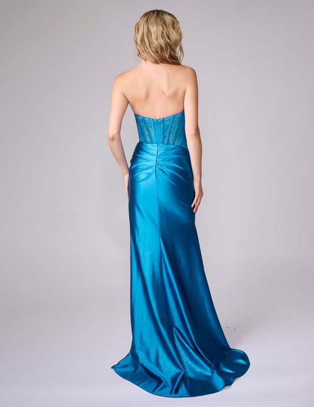 Blonde woman wearing a strapless teal prom dress with a fitted bodice and flowing skirt standing facing away