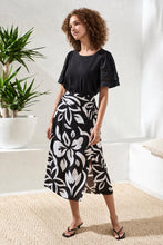 Woman wearing a black top and Tribal Printed Wrap‑Front Pull‑On Midi Skirt with bold white floral pattern in bright room