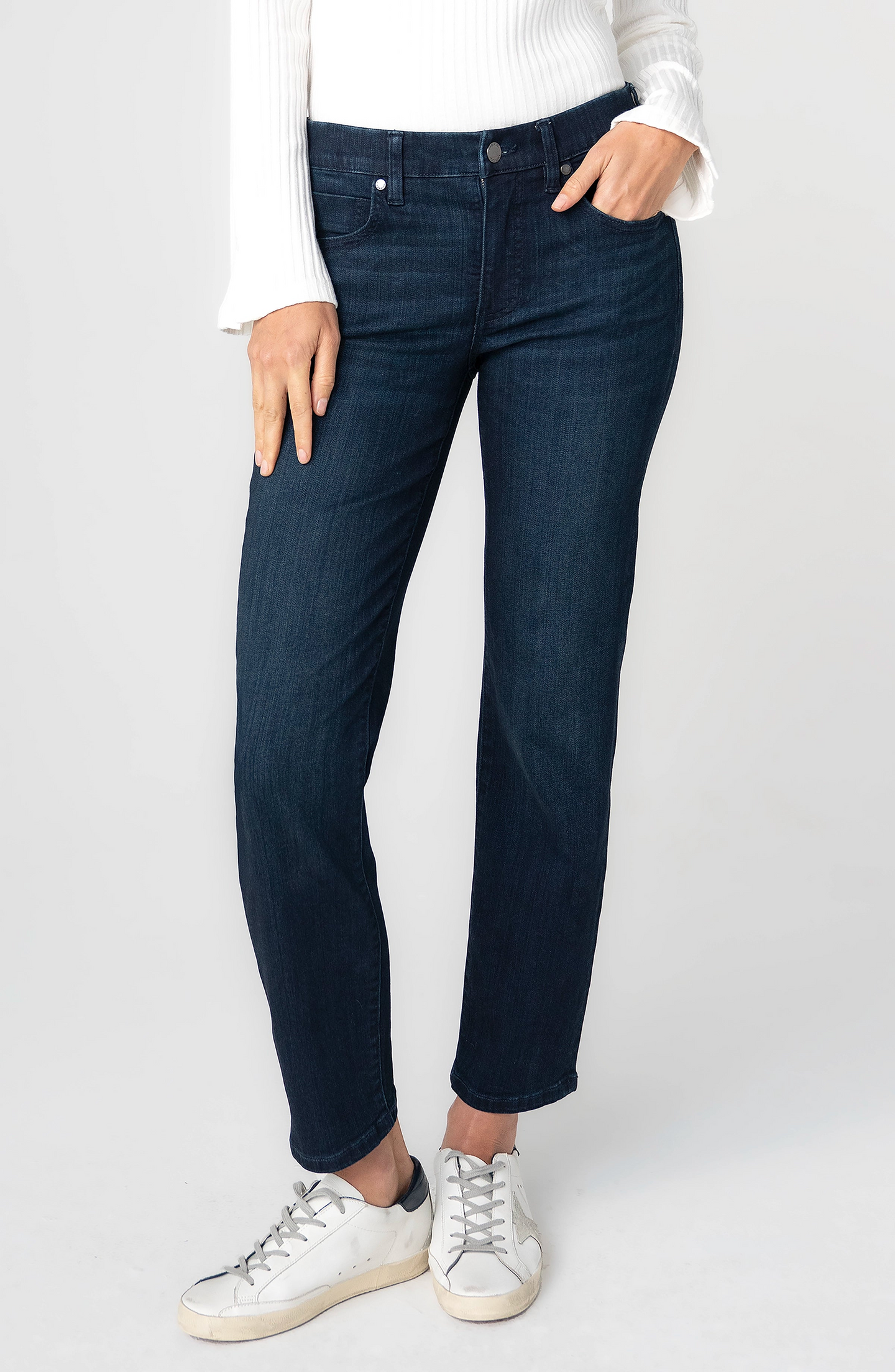 Woman wearing Petunia Blue Rowan Low Rise Comfort Waist Slim 28” Ins jeans by liverpool with white sneakers and white top.