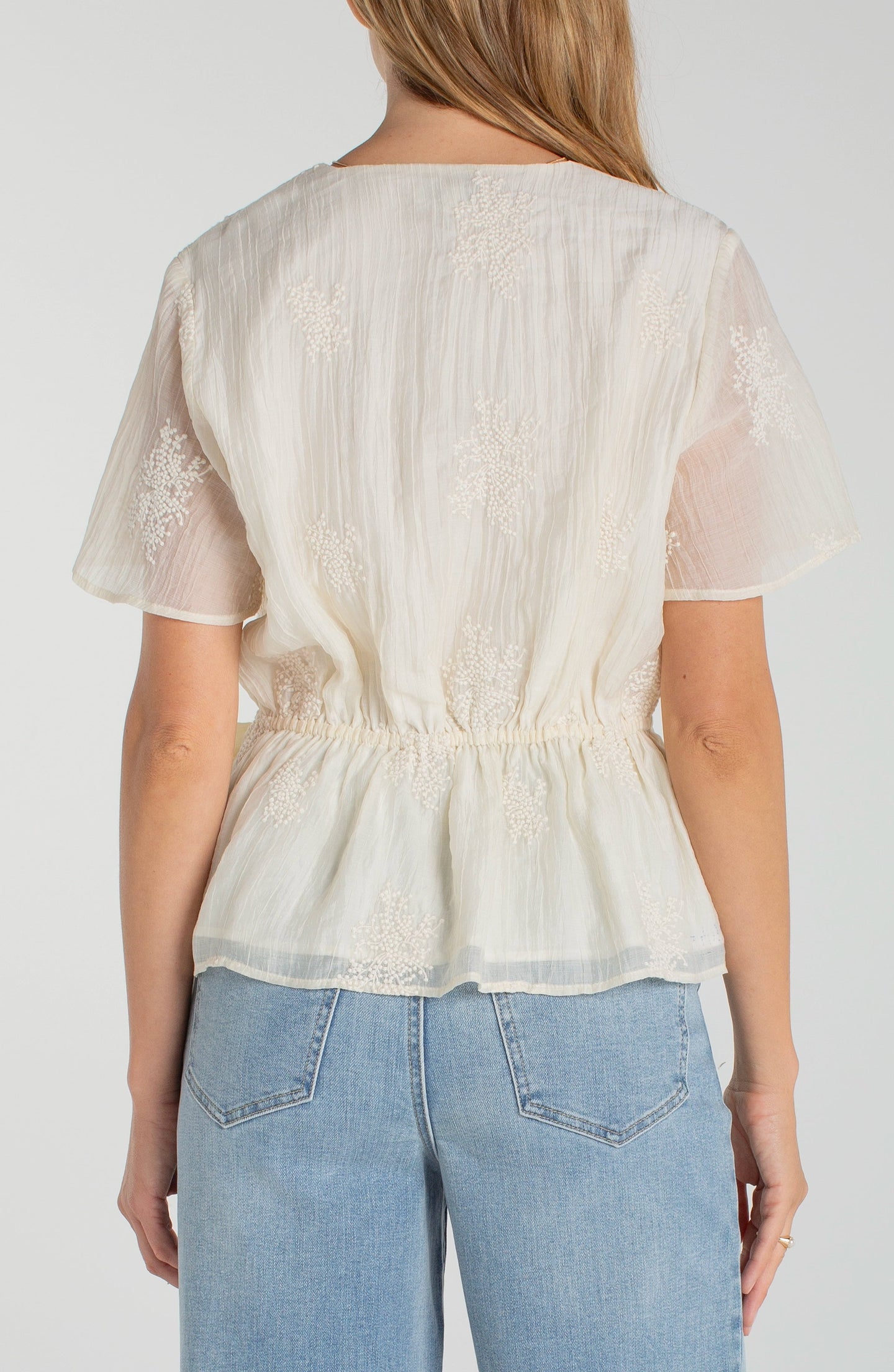 Back view of woman wearing Cream Short Sleeve Wrap Front Woven Top w/ Tie by liverpool with floral texture and light blue jeans