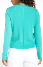 Back view of a woman wearing a waterfall teal long sleeve crew neck sweater by liverpool with white pants