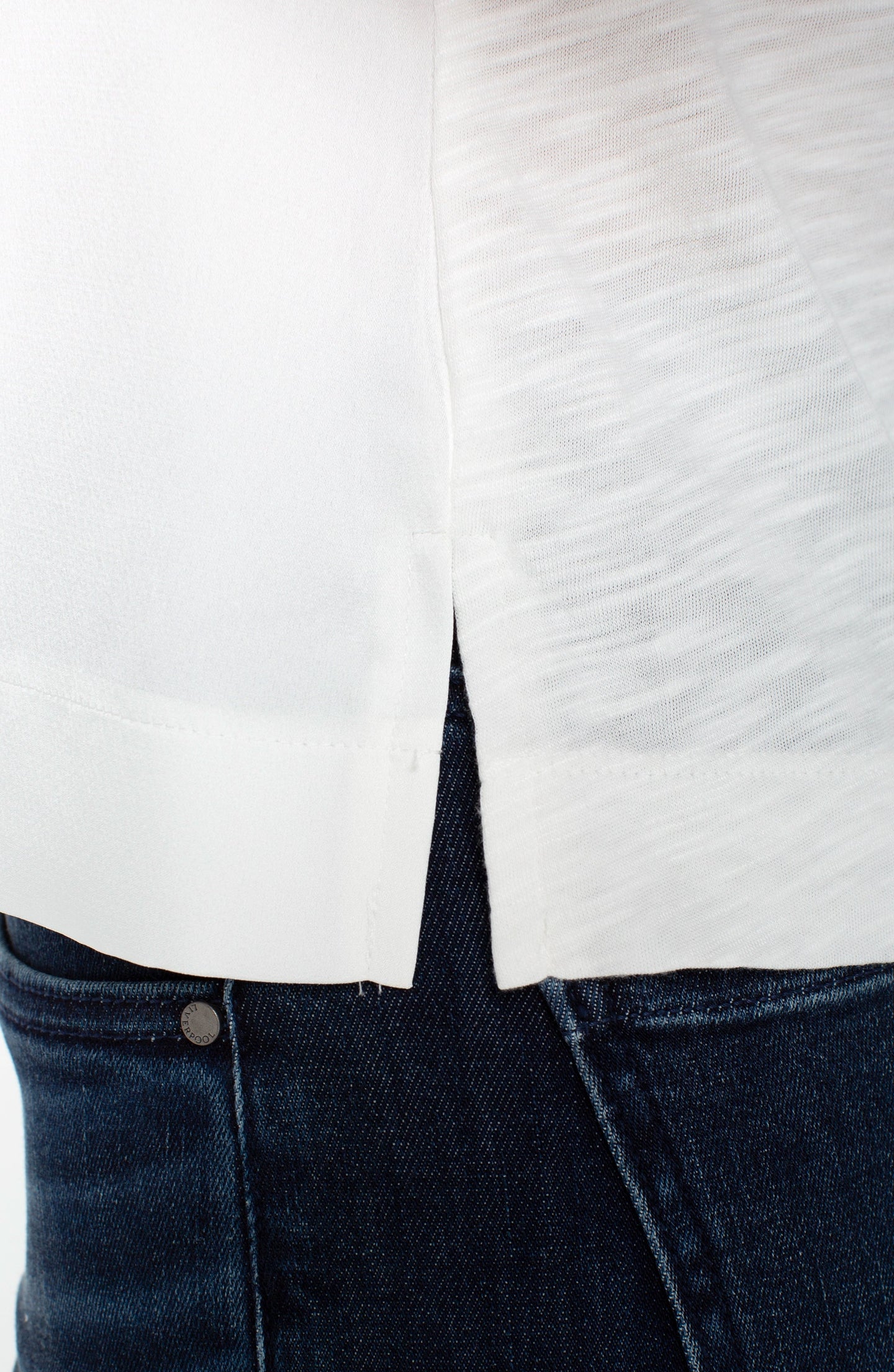 Close-up of side slit detail on whipped cream sleeveless V-neck woven-to-knit tank by liverpool over dark denim jeans.