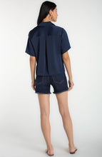 Woman wearing a Dark Navy Short Sleeve Camp Collar Woven Blouse by liverpool, paired with denim shorts, shown from the back.