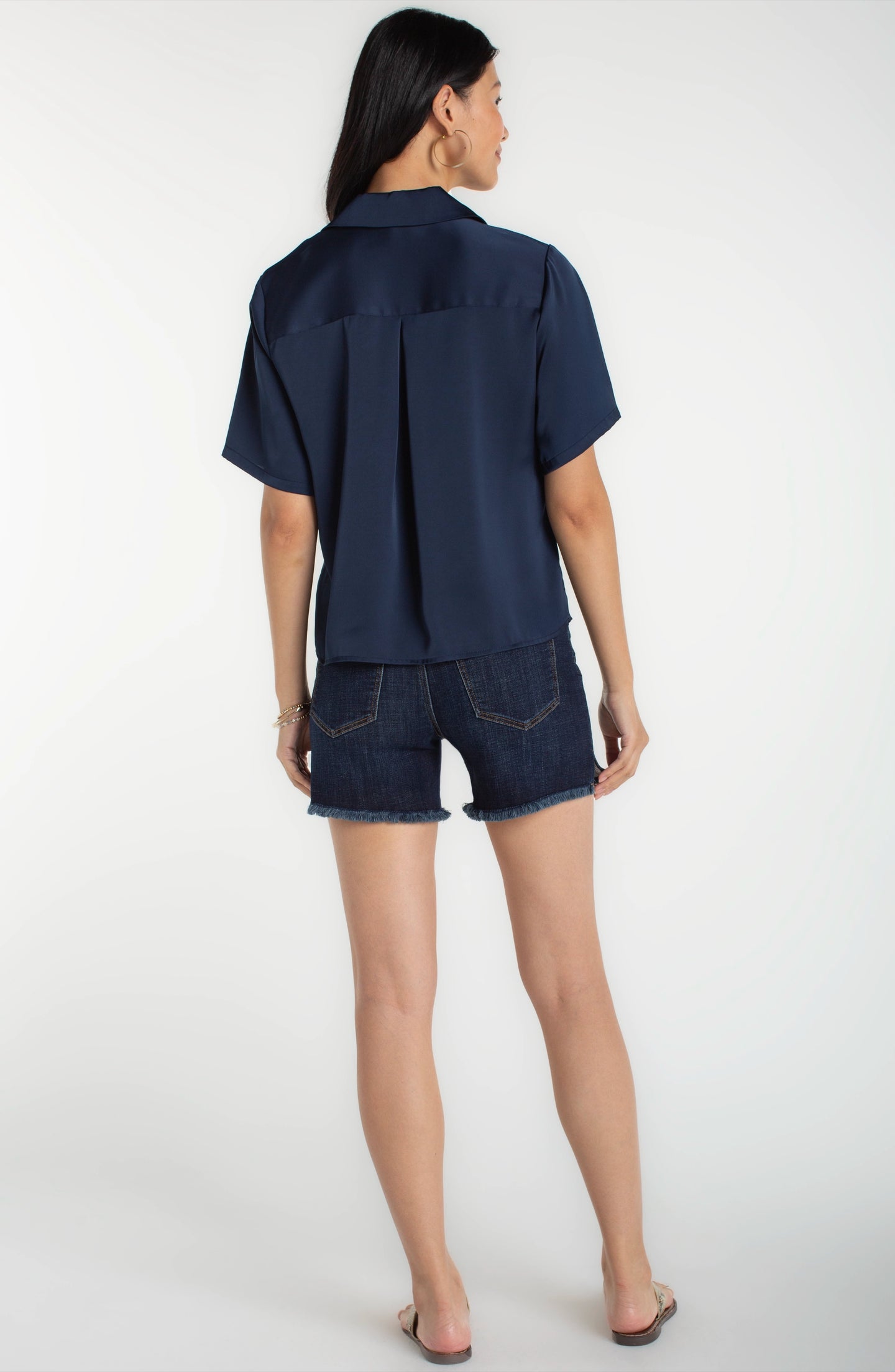 Woman wearing a Dark Navy Short Sleeve Camp Collar Woven Blouse by liverpool, paired with denim shorts, shown from the back.