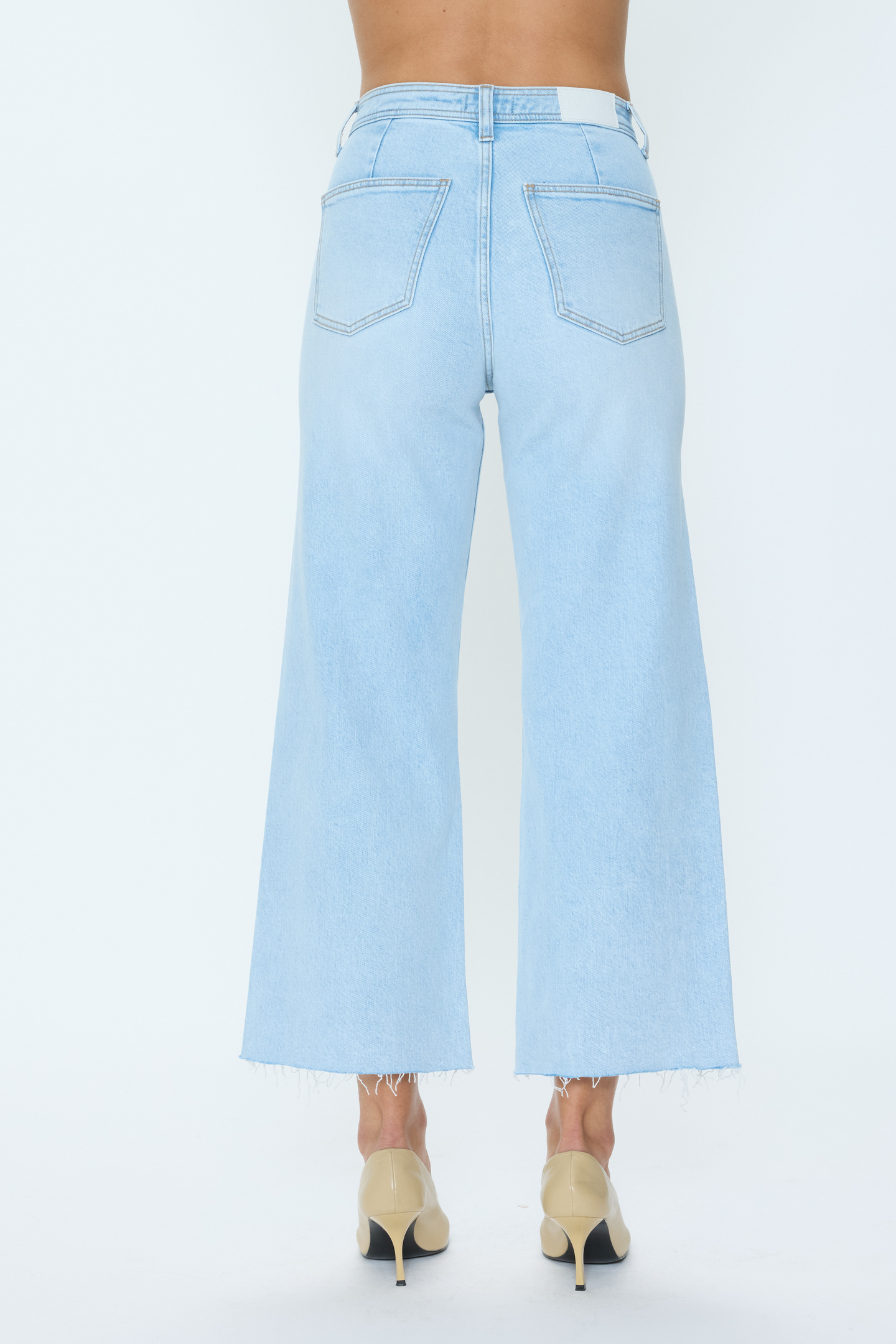 Back view of light wash denim jeans paired with beige heels, styled with the Eternal Penny Crop by pistola.