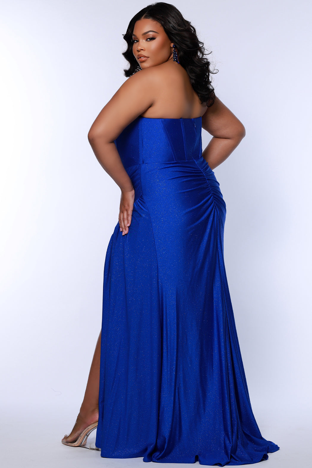 Elegant plus-size model wearing Sydney's Closet Prom Dress Style SC7412 in sparkling sapphire blue, back view