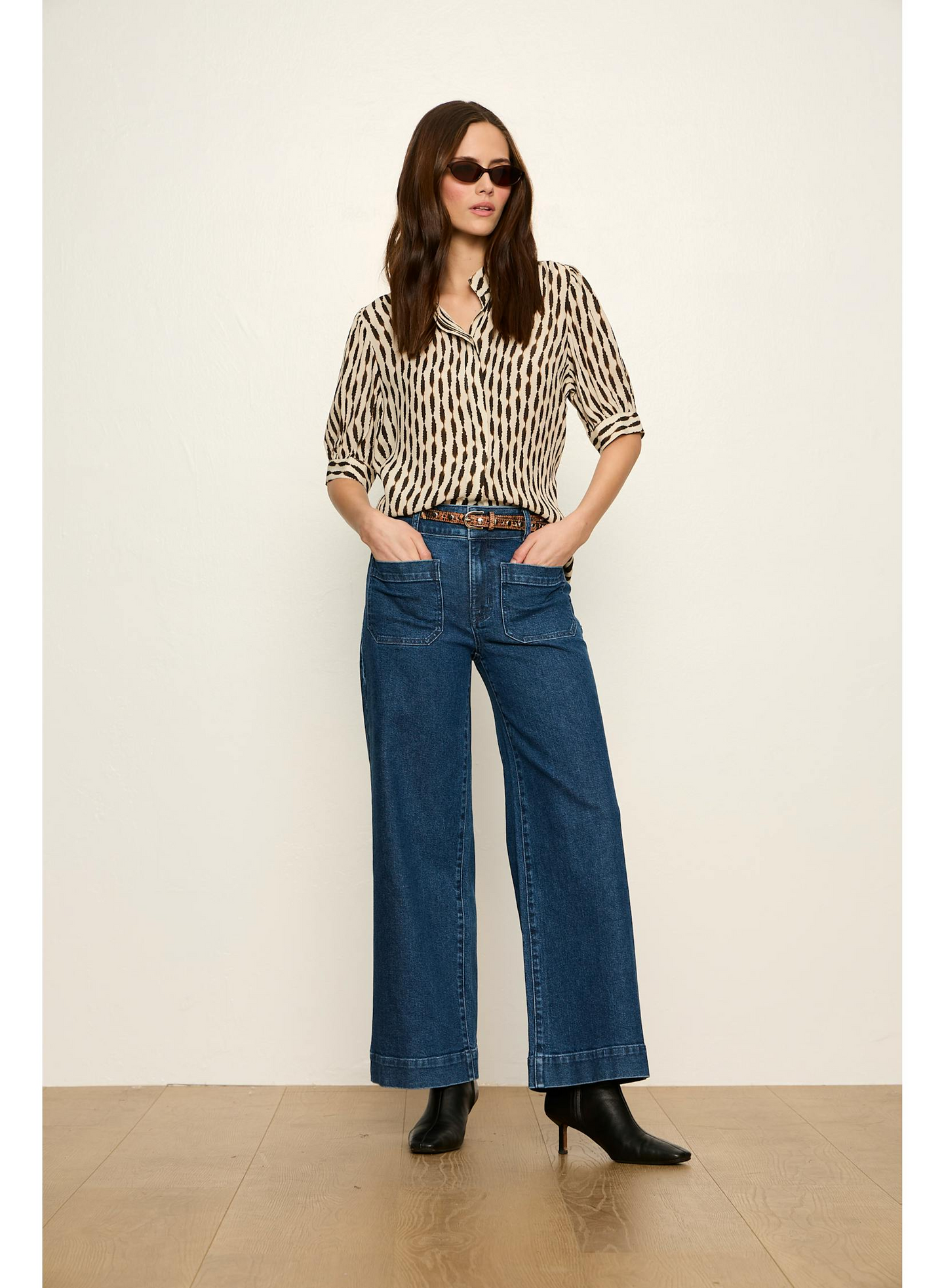 Woman wearing Sanctuary Inkblot Eden Button Blouse with dark sunglasses, tucked into wide-leg denim jeans and black boots.
