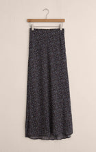 Floral maxi skirt with small blue and brown petals pattern hanging on wooden hanger against beige wall