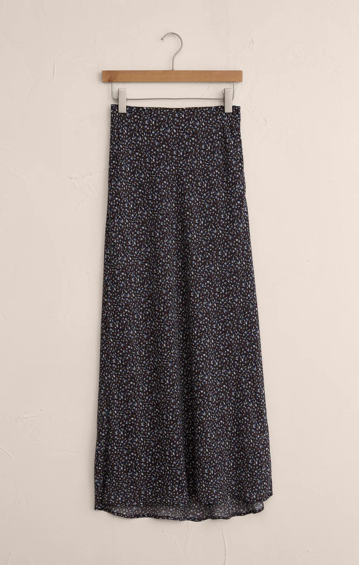 Floral maxi skirt with small blue and brown petals pattern hanging on wooden hanger against beige wall