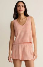 Woman wearing a pink pleated top and shorts set against a beige background