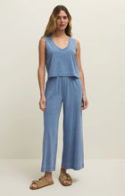 Woman wearing Z Supply Scout Jersey Denim Pant in soft blue with wide leg and elastic waistband styled with tan sandals