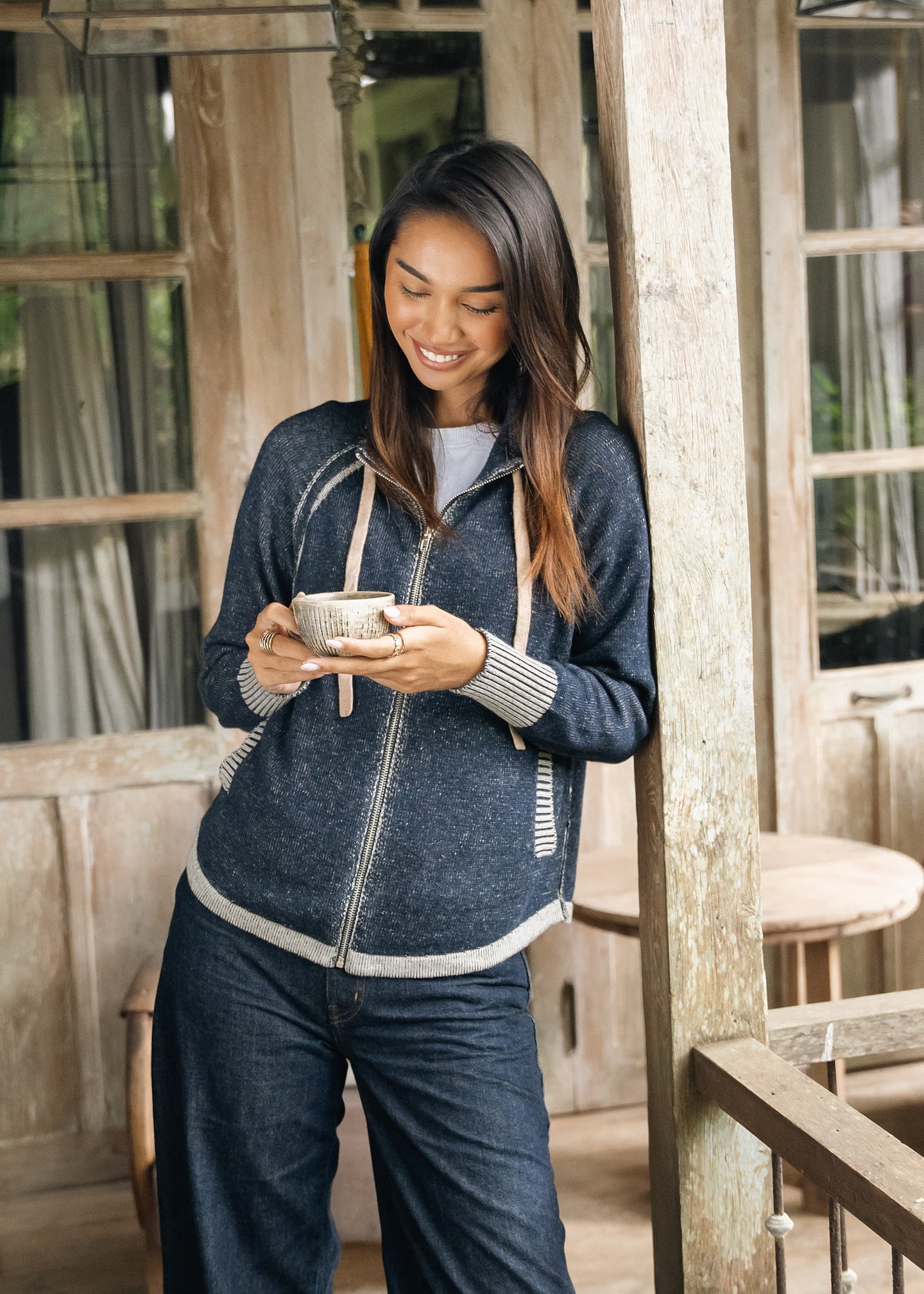 zaket & plover Denim Cardigan worn by a woman on a rustic porch